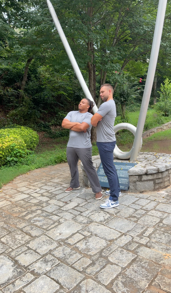 Two TLC members posing back to back by a campus sculpture