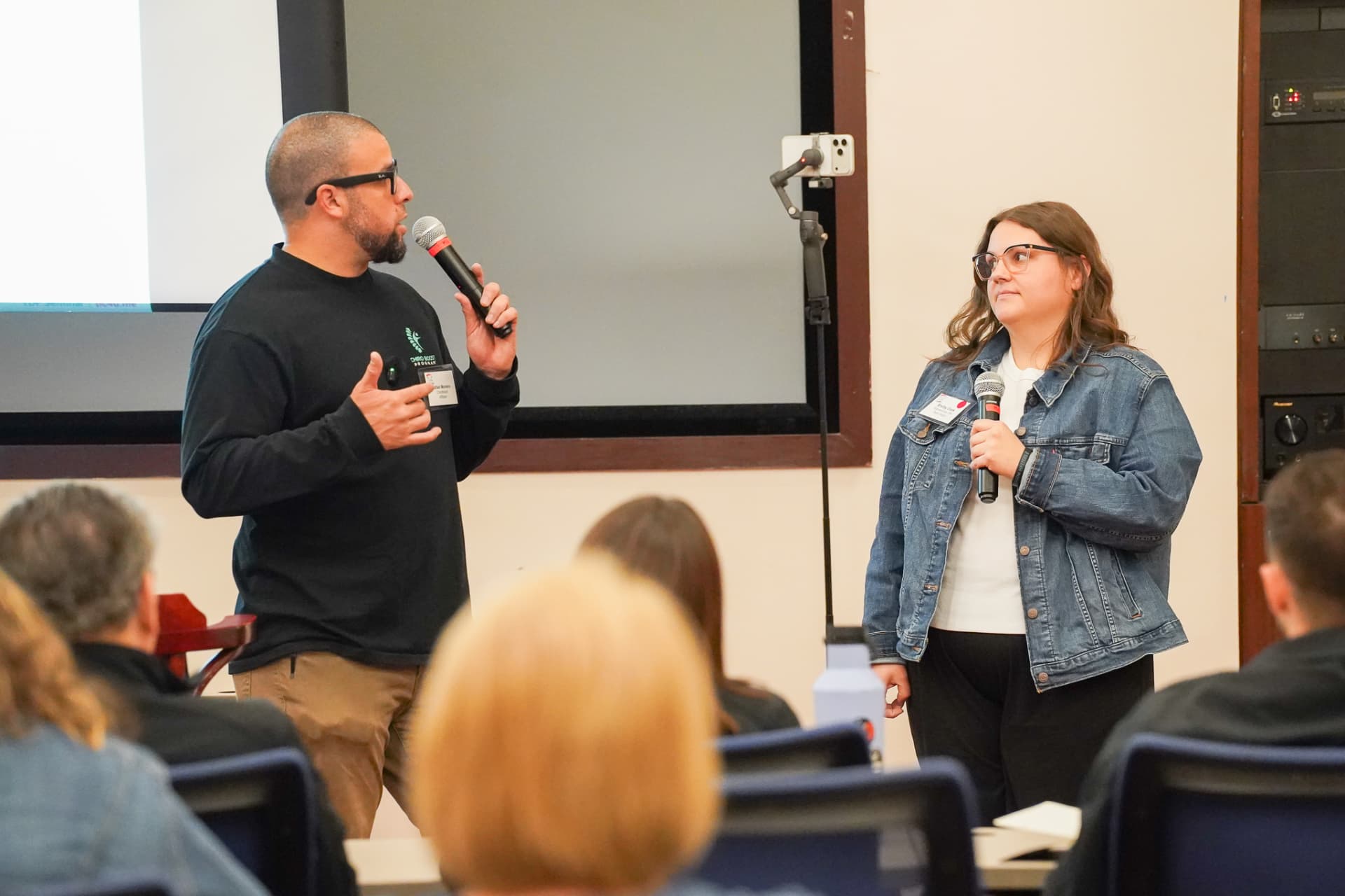 TLC members speaking with microphones at the front of a seminar room