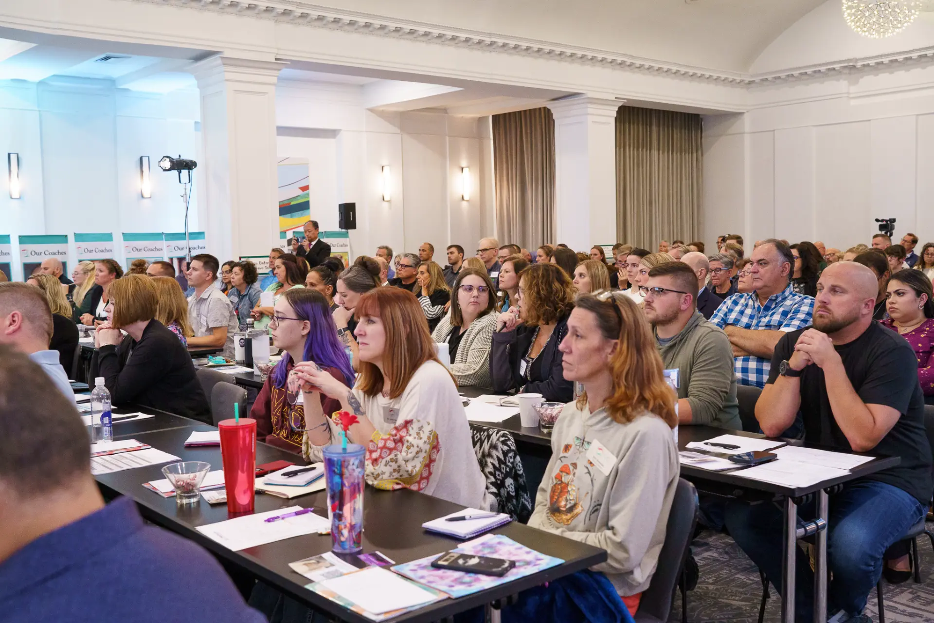 A packed seminar room of TLC members seated at tables during a live event