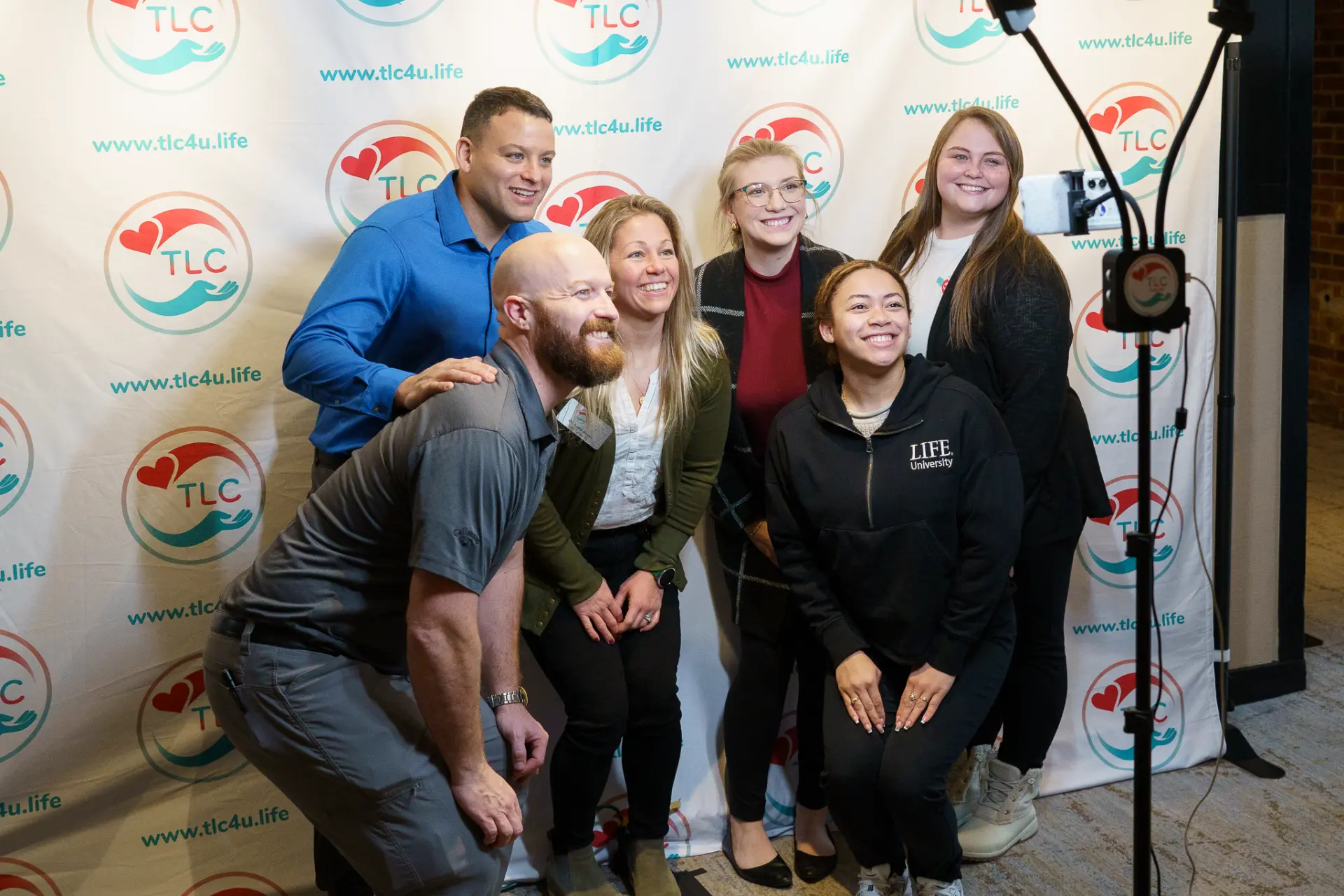 TLC members posing together in front of a TLC backdrop
